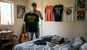 Man sorting band tees in a lived-in bedroom