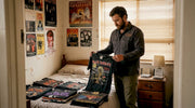 Man sorting vintage metal band shirts on bed