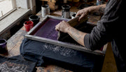 Hands pulling squeegee across silk screen on T-shirt